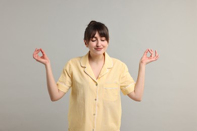 Photo of Woman in pyjama meditating on grey background