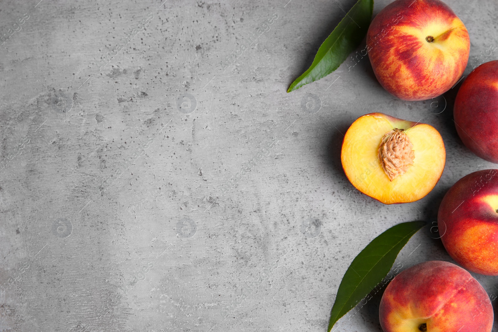 Photo of Fresh peaches and leaves on grey stone surface, top view with space for text