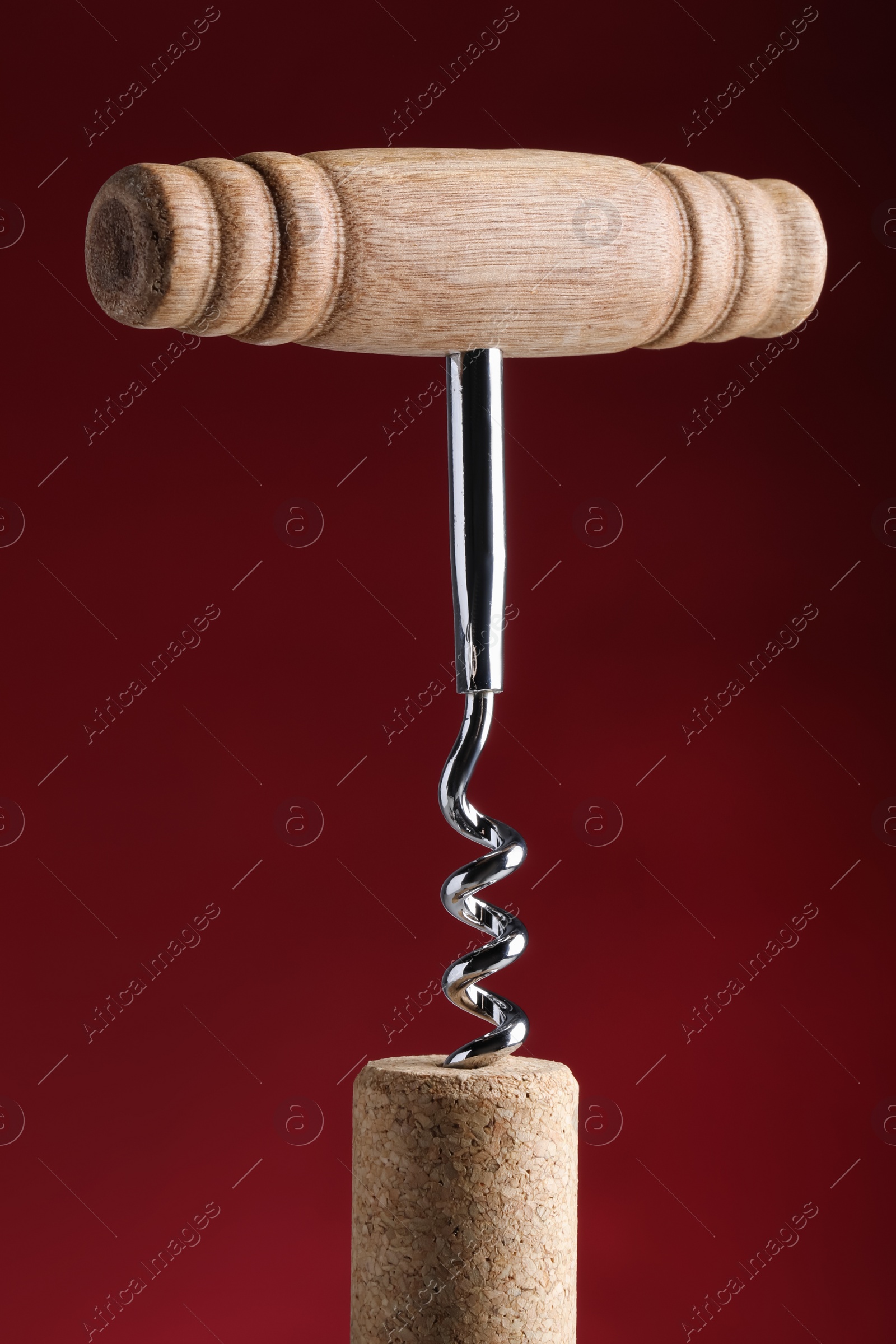 Photo of Corkscrew with cork against dark red background, closeup