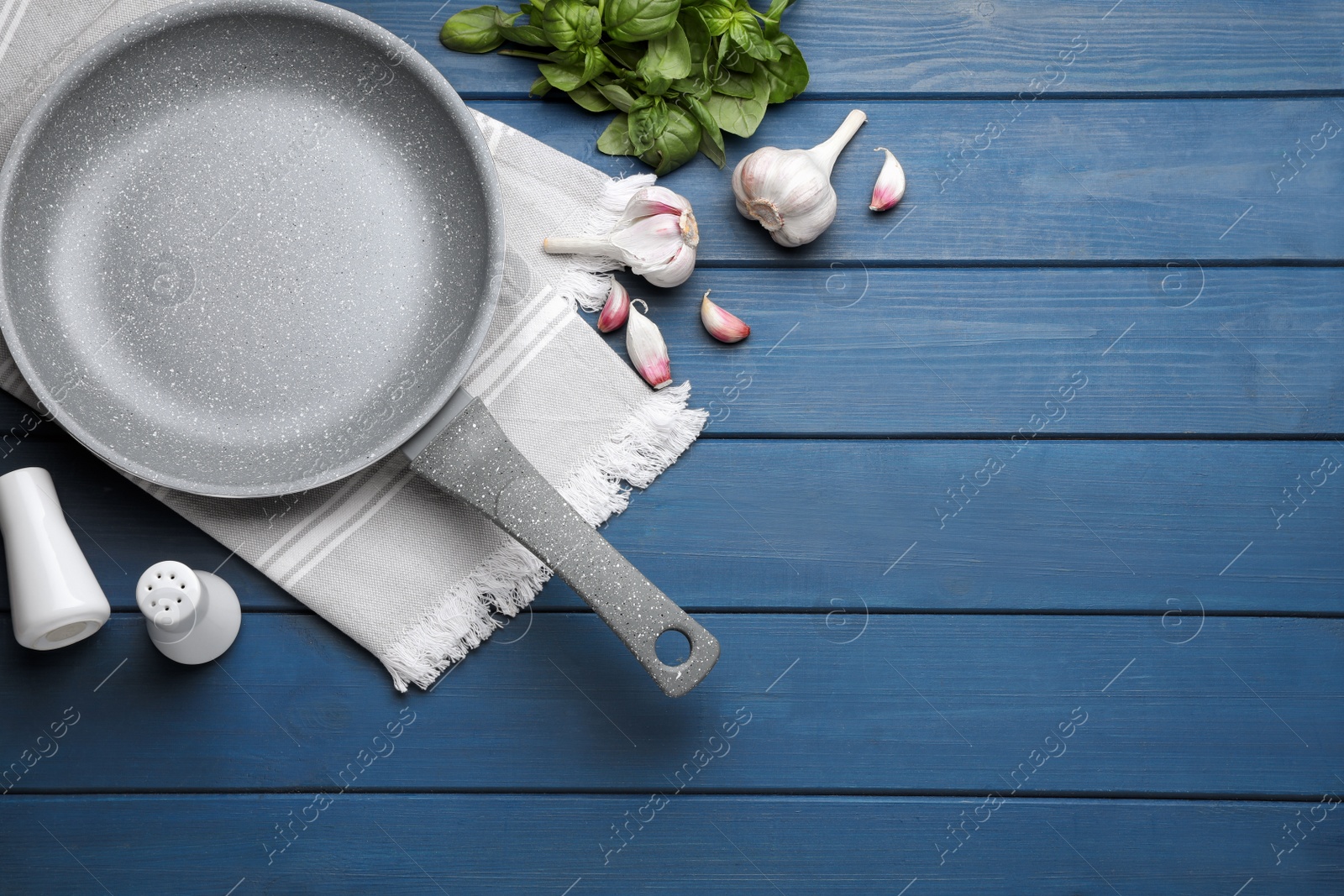 Photo of Empty frying pan, garlic and basil on blue wooden table, flat lay. Space for text