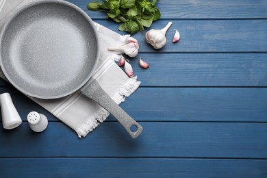 Photo of Empty frying pan, garlic and basil on blue wooden table, flat lay. Space for text