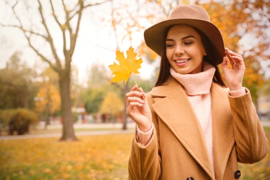 Photo of Young woman in stylish clothes holding yellow leaf outdoors, space for text. Autumn look