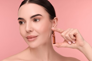 Photo of Beautiful young woman holding skincare ampoule on pink background