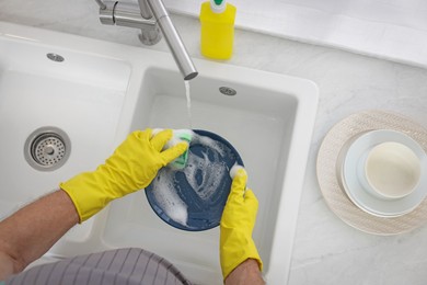 Man in protective gloves washing plate above sink indoors, top view