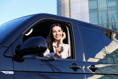 Photo of Young woman with key sitting in car outdoors. Buying new auto