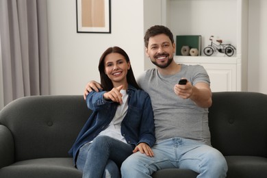 Photo of Happy couple watching show at home. Man changing TV channels with remote control