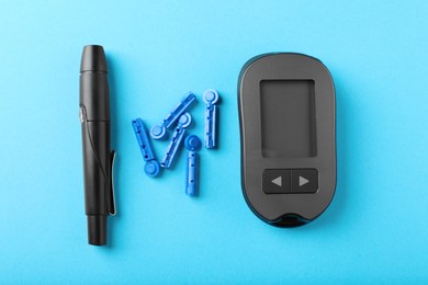 Digital glucometer, lancets and pen on light blue background, flat lay. Diabetes control