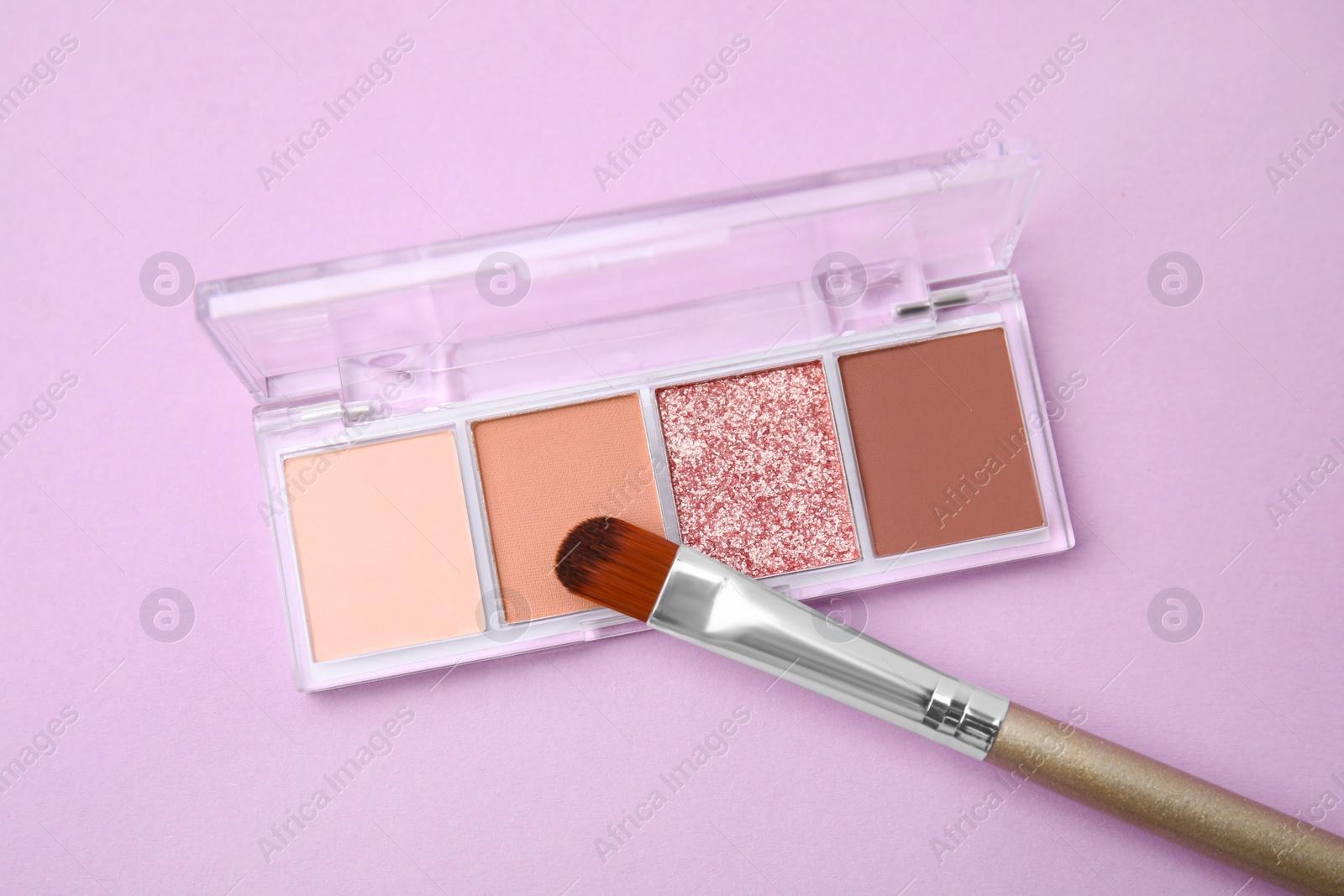 Photo of Beautiful eye shadow palette and brush on lilac background, top view