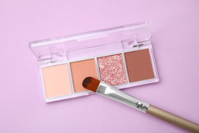 Beautiful eye shadow palette and brush on lilac background, top view