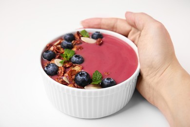Woman holding bowl of delicious smoothie with fresh blueberries and granola on white background, closeup