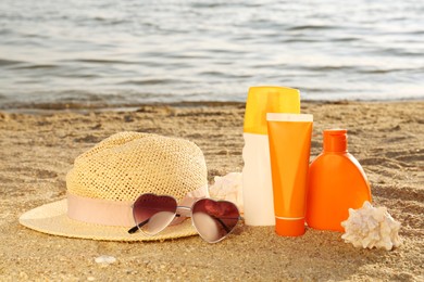 Photo of Sun protection products and beach accessories on sand near sea, space for text