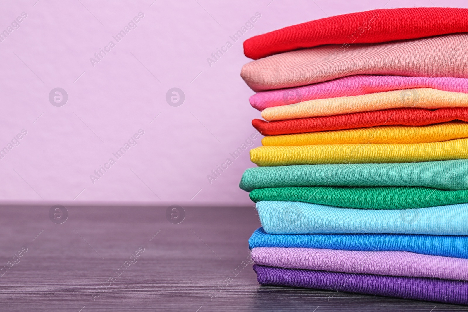 Photo of Stack of colorful t-shirts on table against color background