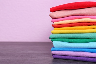 Photo of Stack of colorful t-shirts on table against color background