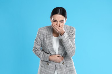 Photo of Woman in office suit suffering from stomach ache and nausea on light blue background. Food poisoning