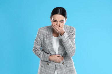 Woman in office suit suffering from stomach ache and nausea on light blue background. Food poisoning