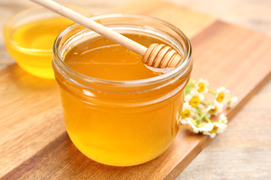 Tasty honey in glass jar on wooden board, closeup