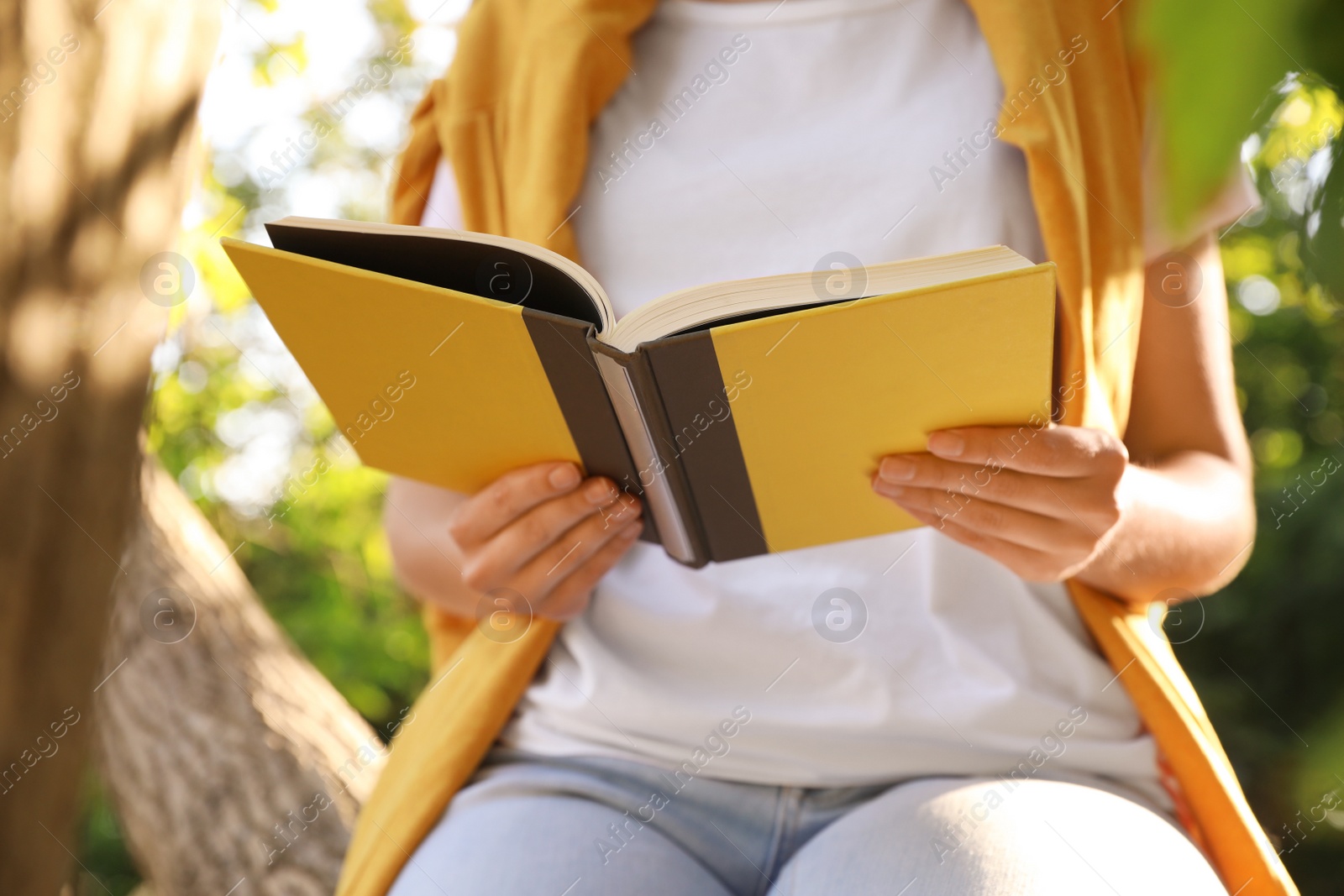 Photo of Young woman reading book near tree in park, closeup