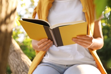 Photo of Young woman reading book near tree in park, closeup