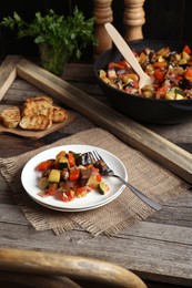 Delicious ratatouille served with bread on wooden table