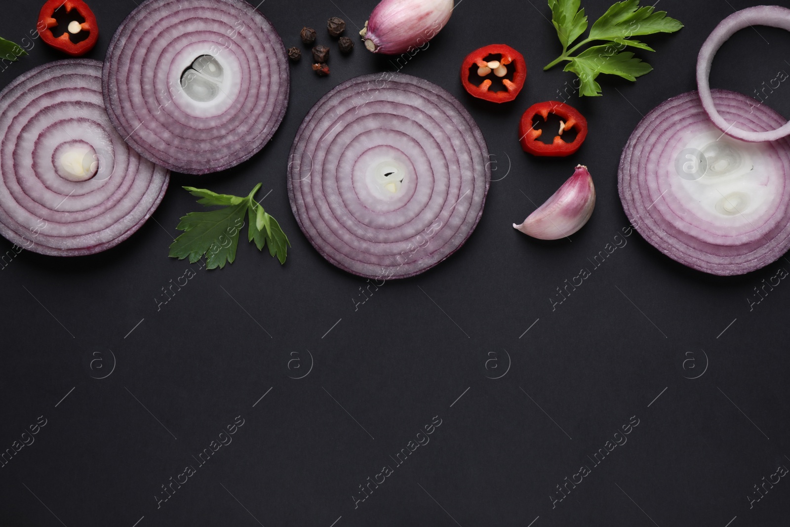 Photo of Flat lay composition with slices of onion and spices on black background. Space for text