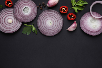 Photo of Flat lay composition with slices of onion and spices on black background. Space for text