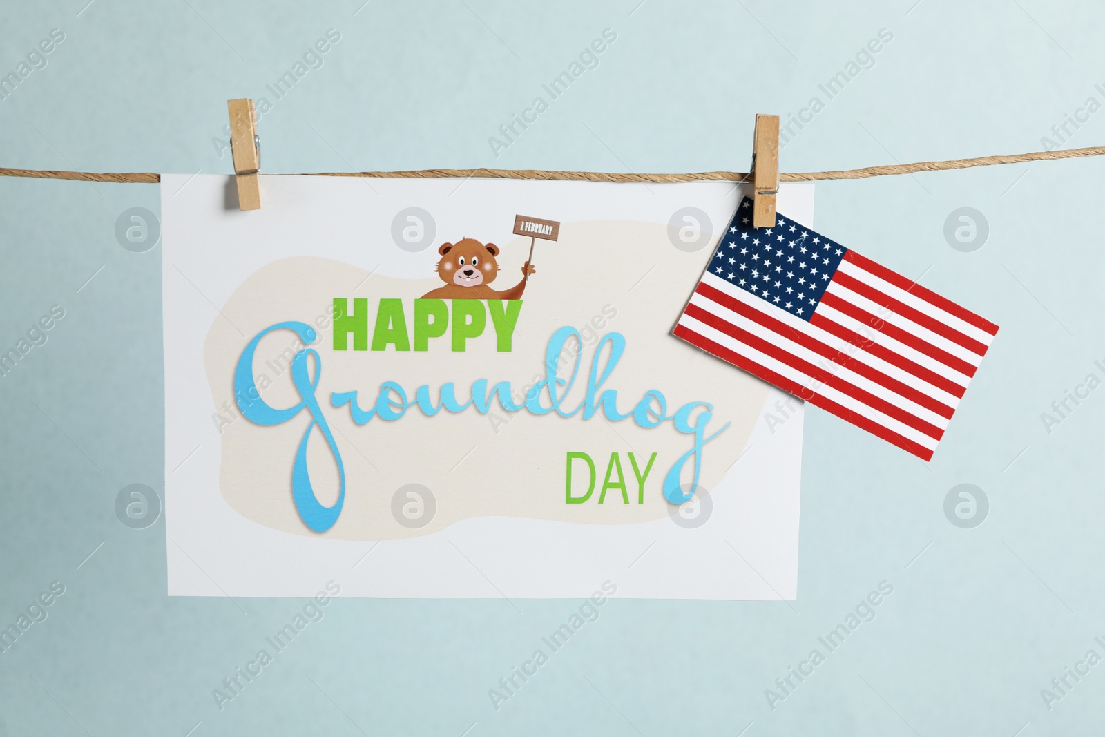 Photo of Happy Groundhog Day greeting card and American flag hanging on light background