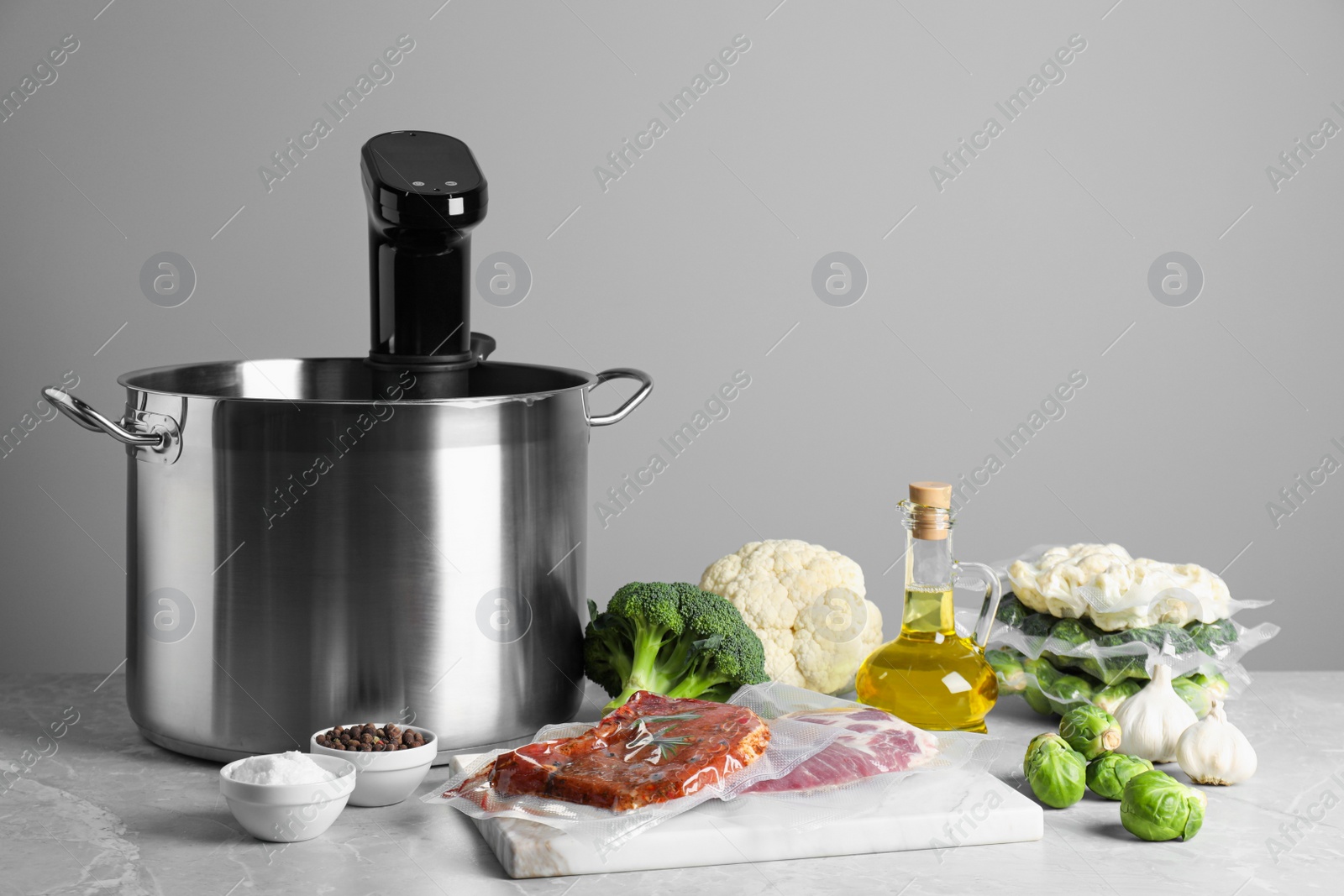 Photo of Thermal immersion circulator in pot and ingredients on light grey table, space for text. Vacuum packing for sous vide cooking