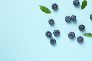 Photo of Tasty fresh blueberries with green leaves on light blue background, flat lay. Space for text