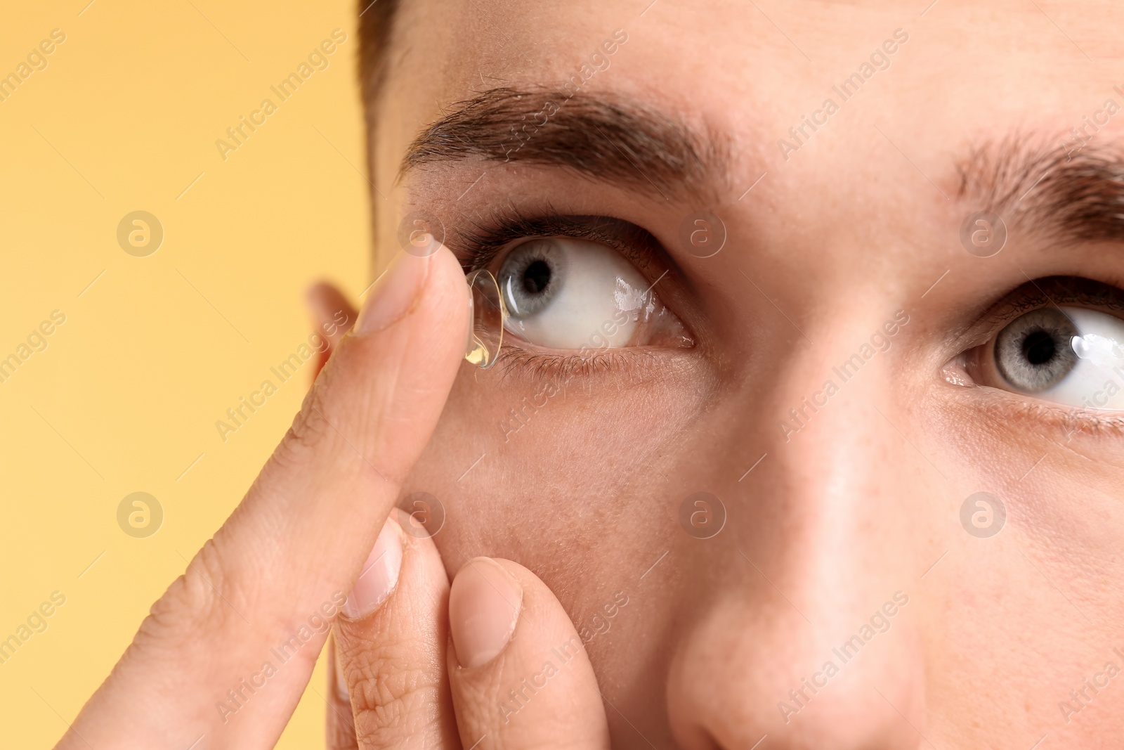 Photo of Young man putting contact lens in his eye on color background