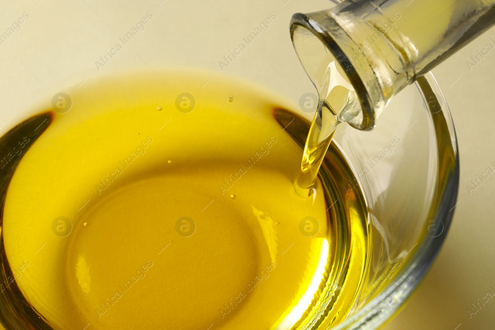 Photo of Pouring cooking oil from bottle into bowl on white background, closeup