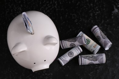 Photo of Financial savings. Piggy bank and dollar banknotes on black textured table, flat lay