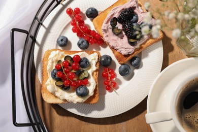 Photo of Cup of coffee near sandwiches with cream cheese and berries on tray, flat lay