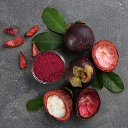 Photo of Purple mangosteen powder and fruits on grey table, flat lay