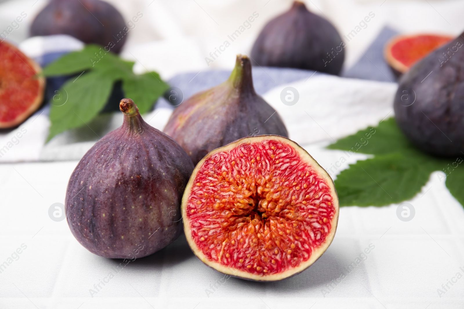 Photo of Fresh ripe purple figs on white tiled table, closeup