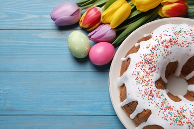 Glazed Easter cake with sprinkles, painted eggs and tulips on blue wooden table, flat lay. Space for text