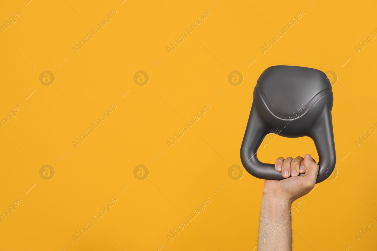 Photo of Man holding kettlebell on orange background, closeup. Space for text