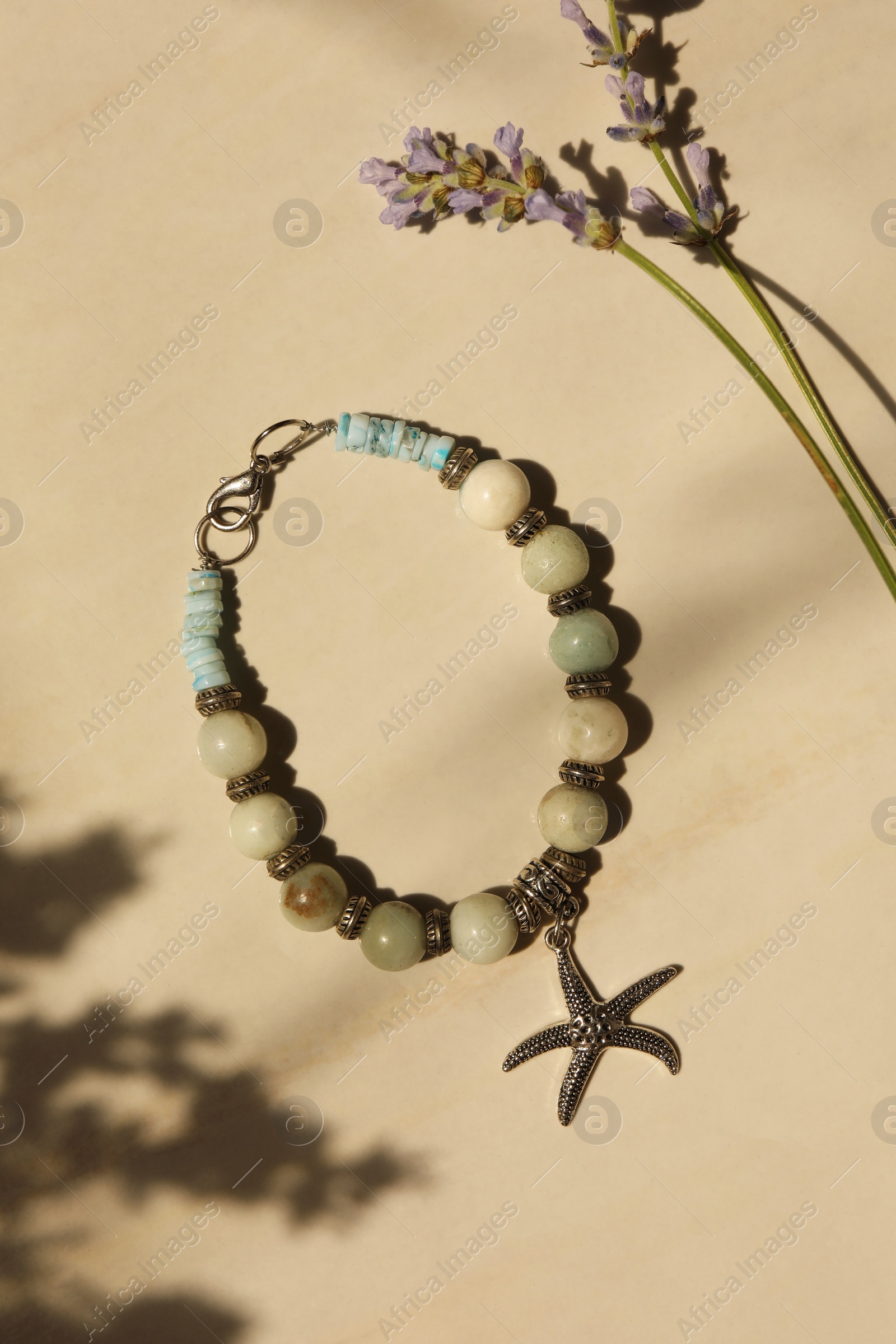 Photo of Beautiful bracelet with different gemstones and lavender flowers on beige background, flat lay