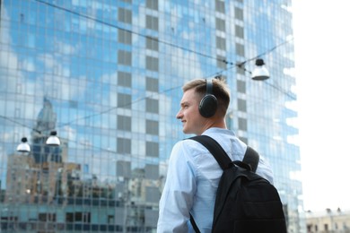 Photo of Smiling man in headphones listening to music outdoors, back view. Space for text