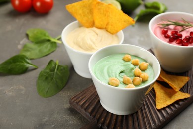 Photo of Different kinds of tasty hummus served with nachos on grey table, space for text