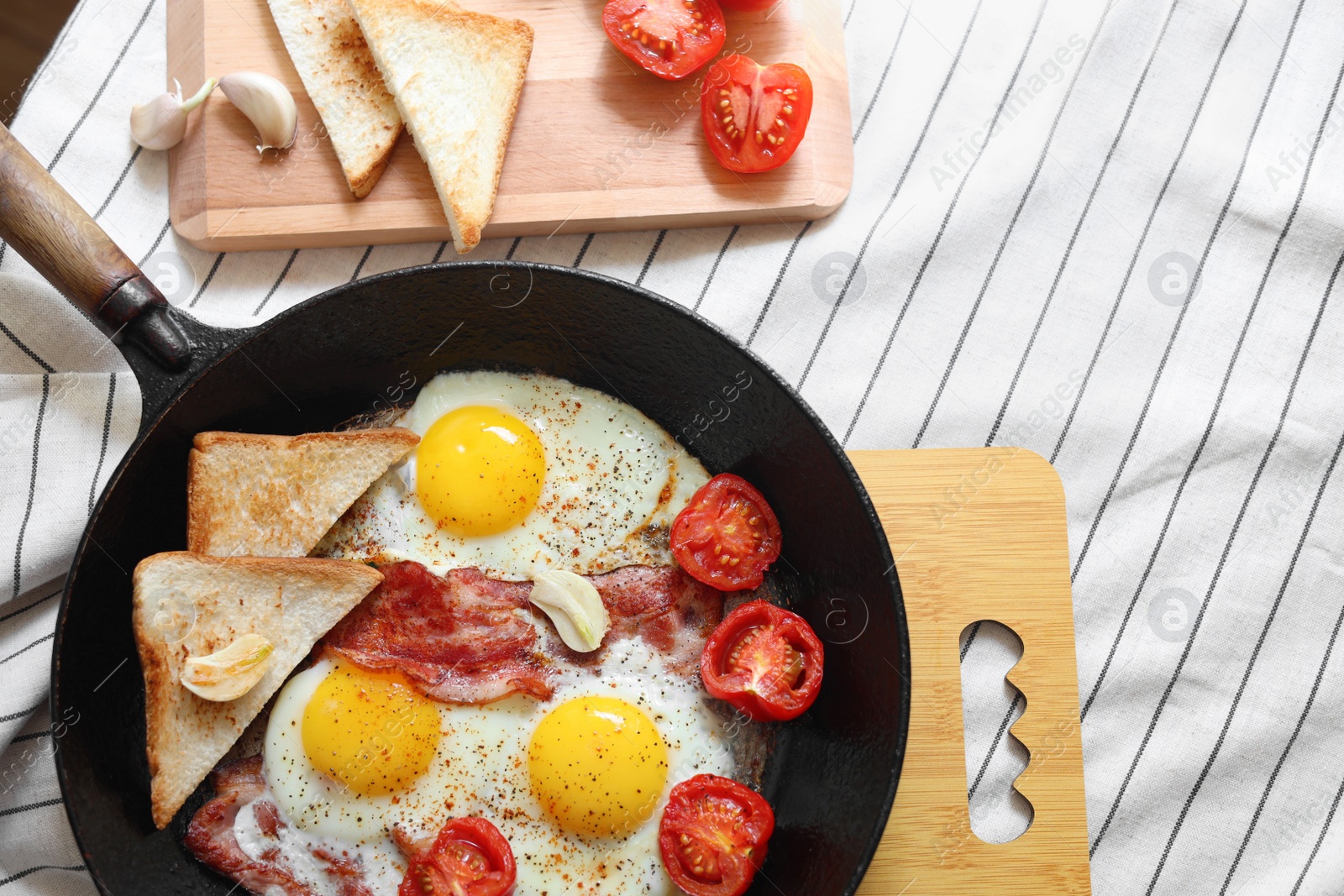 Photo of Delicious fried eggs with bacon and tomatoes in pan on table, flat lay