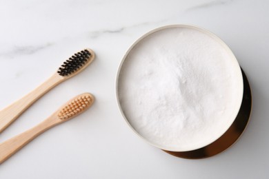 Bamboo toothbrushes and bowl of baking soda on white marble table, flat lay