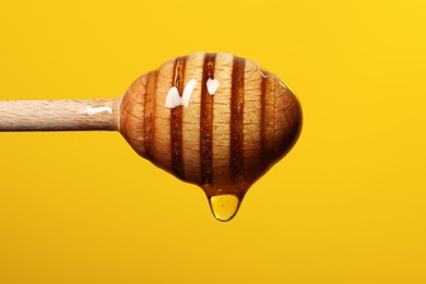 Photo of Pouring honey from dipper against golden background, closeup. Space for text