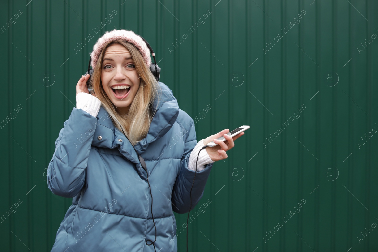 Photo of Young woman with headphones listening to music near color wall. Space for text