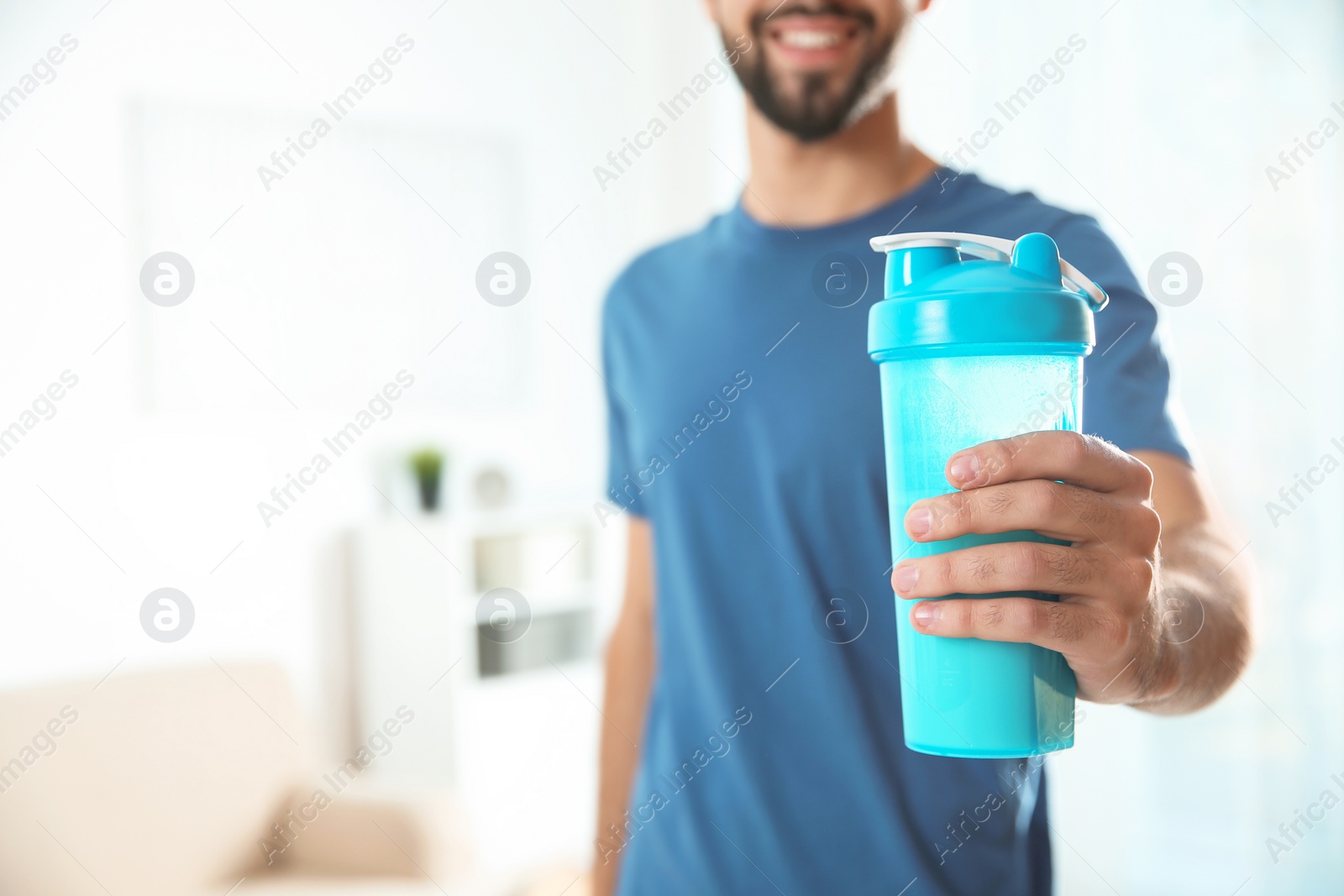 Photo of Young man with bottle of protein shake at home, closeup. Space for text