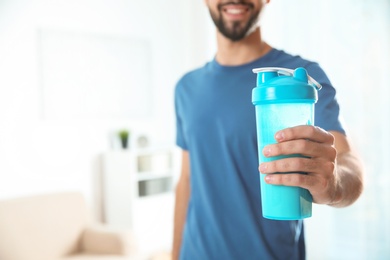 Young man with bottle of protein shake at home, closeup. Space for text