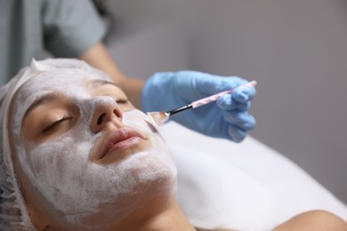 Photo of Cosmetologist applying mask on client's face in spa salon, closeup