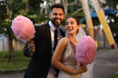 Photo of Happy newlywed couple with cotton candies outdoors