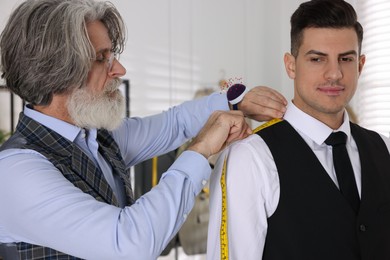Photo of Professional tailor measuring shoulder seam length on client's vest in atelier