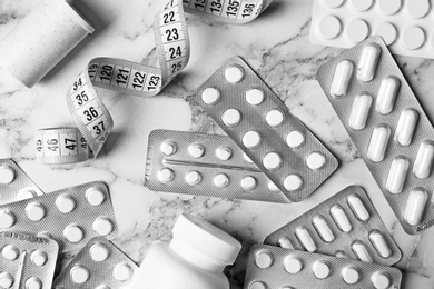 Flat lay composition with weight loss pills and measuring tape on marble background