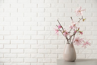 Magnolia tree branches with beautiful flowers in vase on grey table against white brick wall, space for text